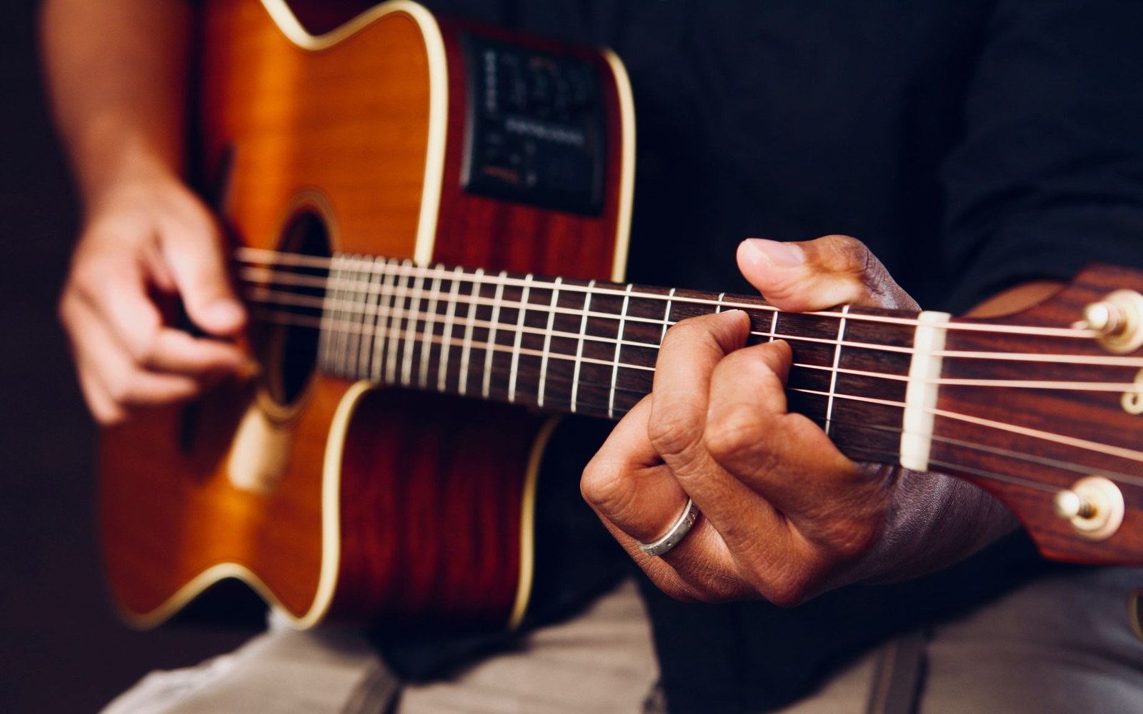 Close-up of hands fretting chords on an acoustic guitar's neck