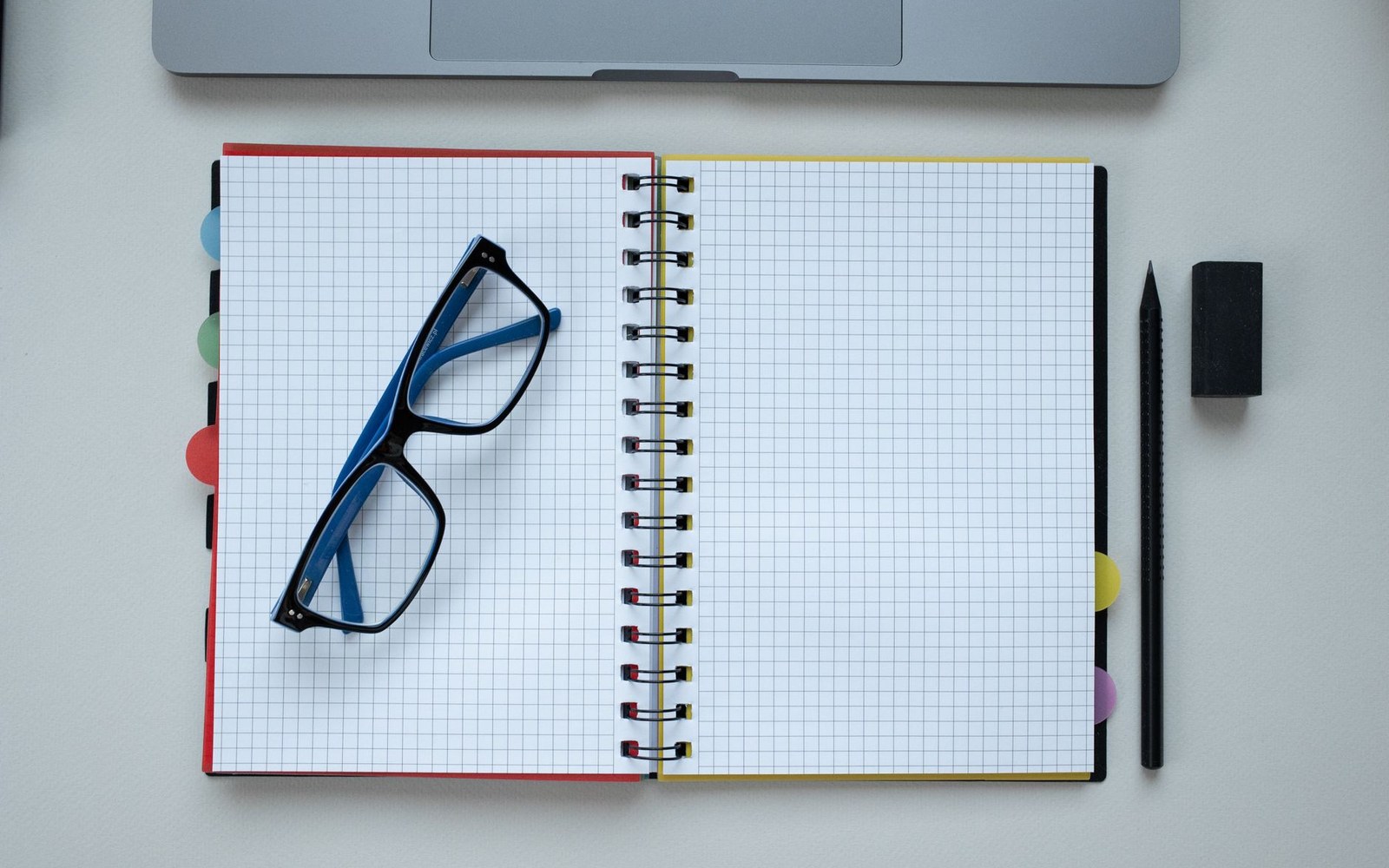 Blue glasses resting on a blank spiral notebook beside a pencil and eraser