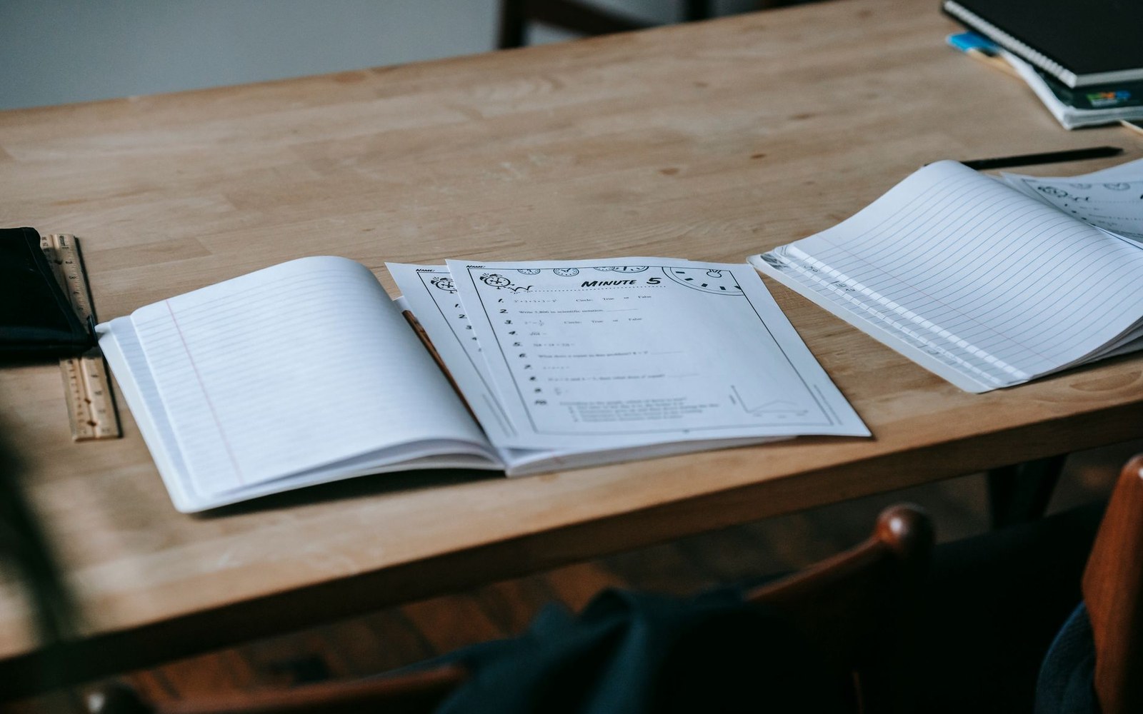 Open notebooks and a math worksheet spread across a wooden desk with a ruler
